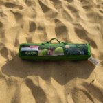 A Coleman Beach Shade carrying case, fully packed, lying on sand.