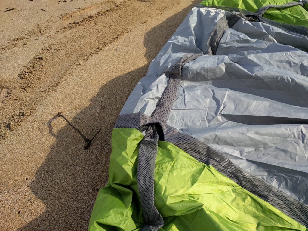 A portion of a beach tent, rolled out in the sand, awaiting setup.