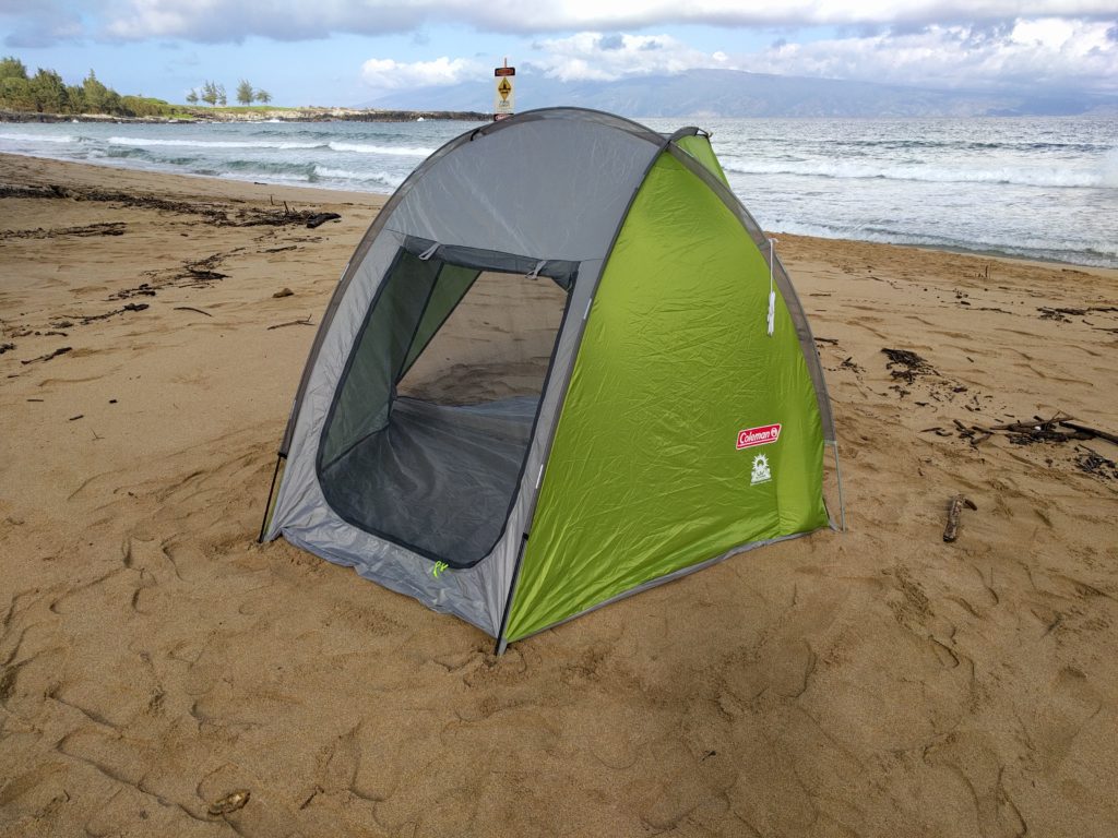 A Coleman Beach Shade set up on a sandy beach with the rear window open. The ocean is visible in the background.