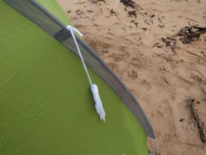 A white rope tether attached to the corner of a beach tent, ready to be secured in the sand with a stake.