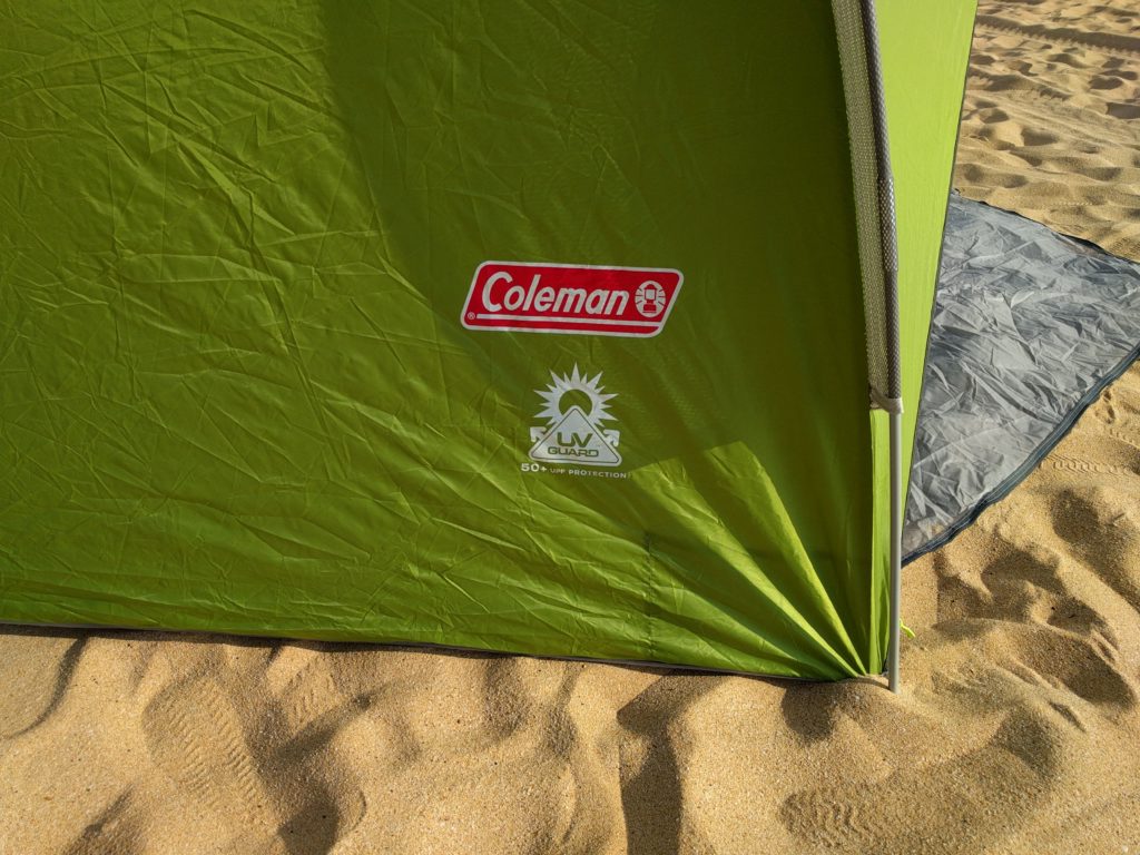 The UV Guard logo on a green Coleman Beach Tent, set up in the sand.