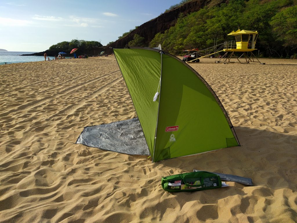 A fully assembled green beach tent, front door open, on a wide, sandy beach.