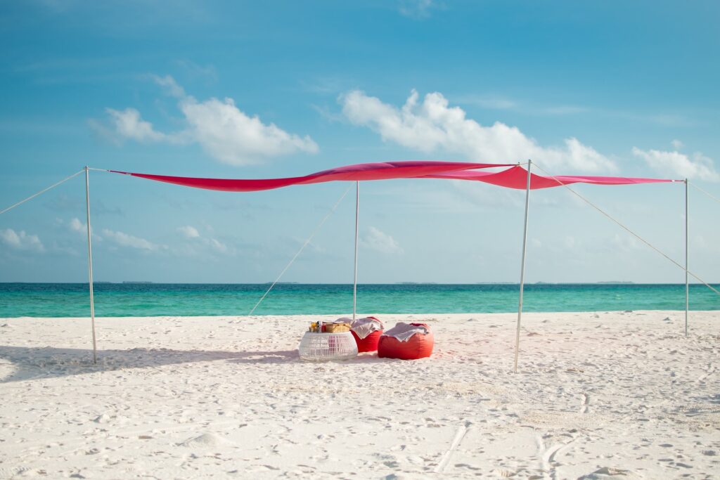 A pink beach canopy suspended above a sandy beach, with the ocean visible in the background.