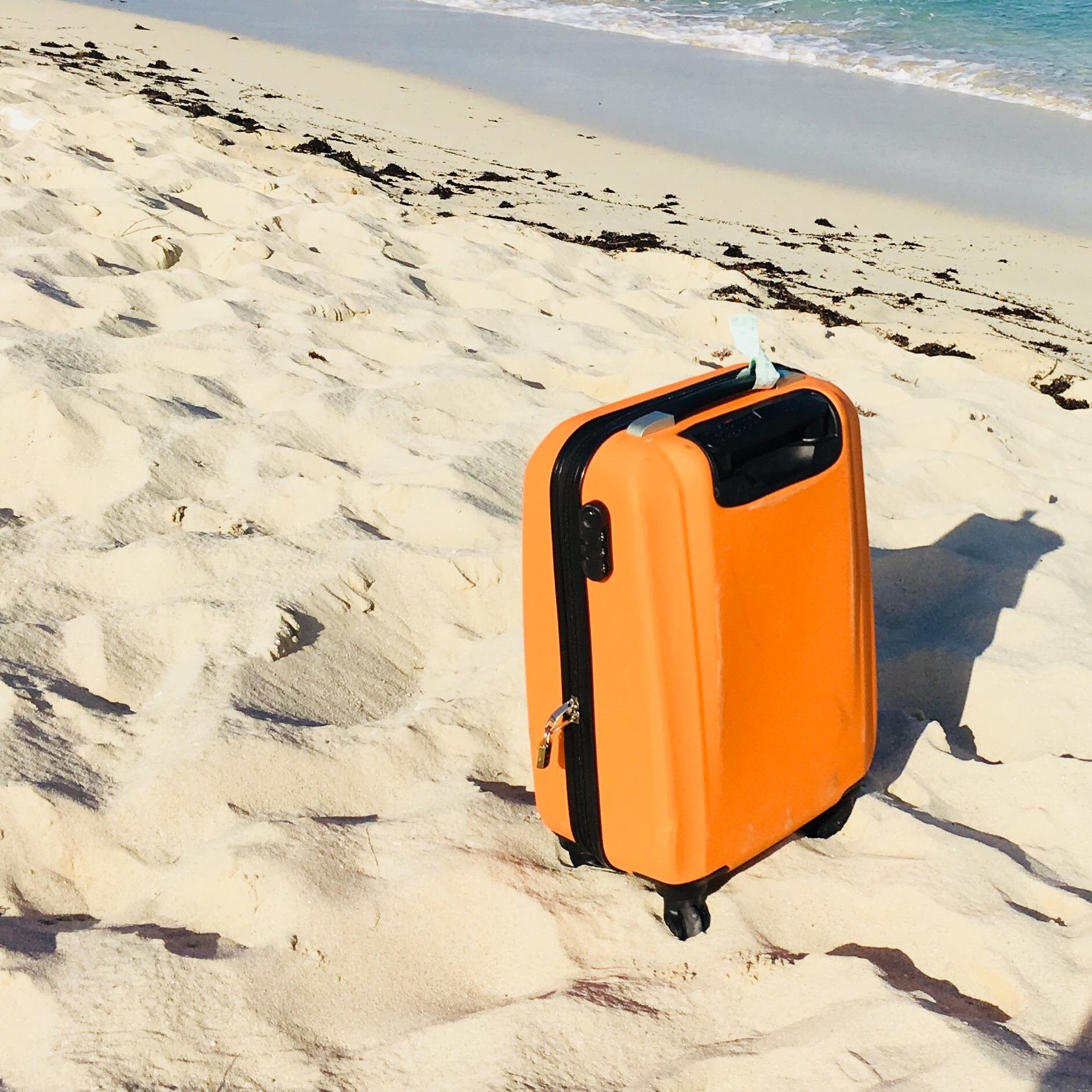 A bright orange suitcase placed on a sandy beach.