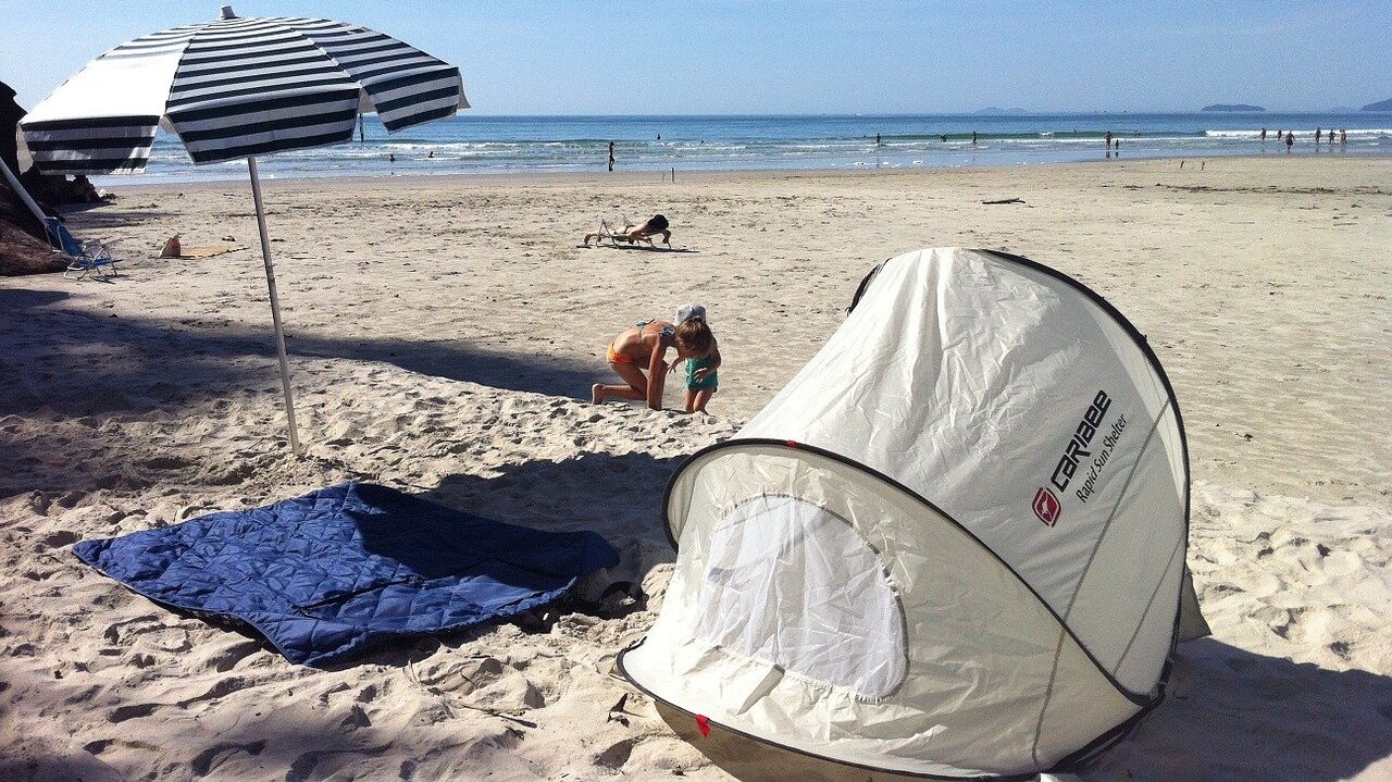 A pop-up beach tent on a sandy beach, with the ocean visible in the background.