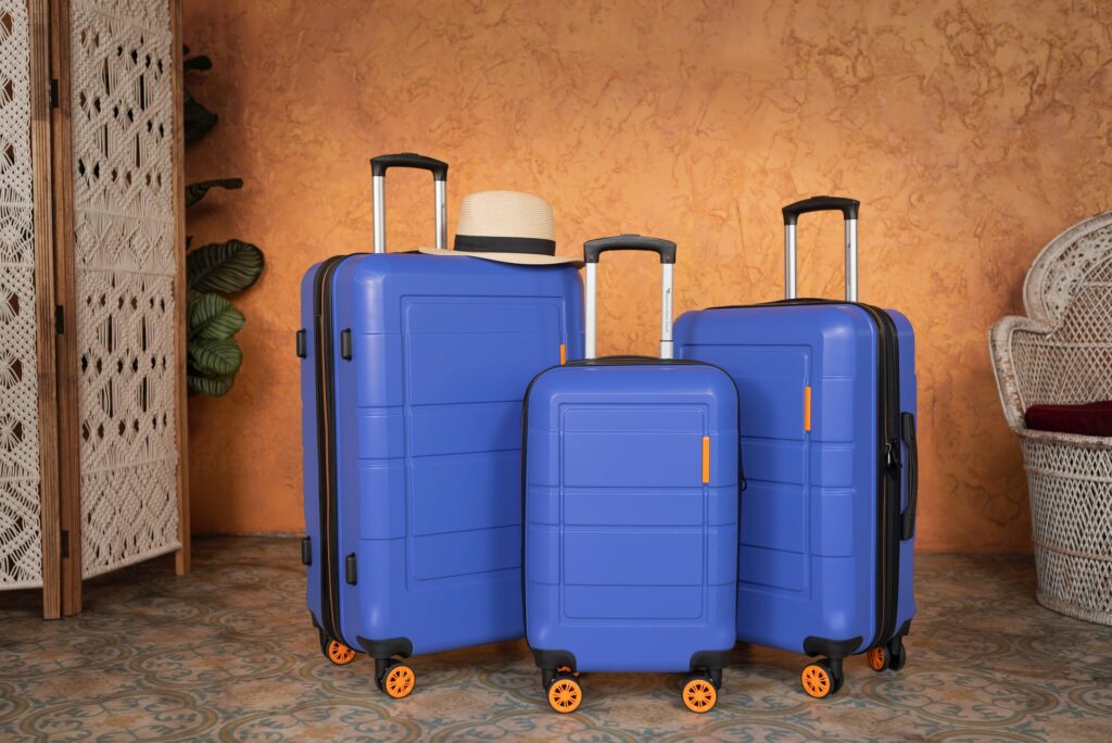 A trio of suitcases ready for a trip. A beach hat sits atop the largest suitcase.